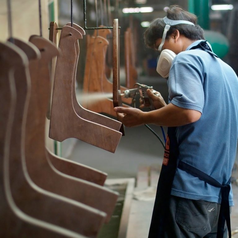 Factory worker spray painting furniture parts at an assembly line